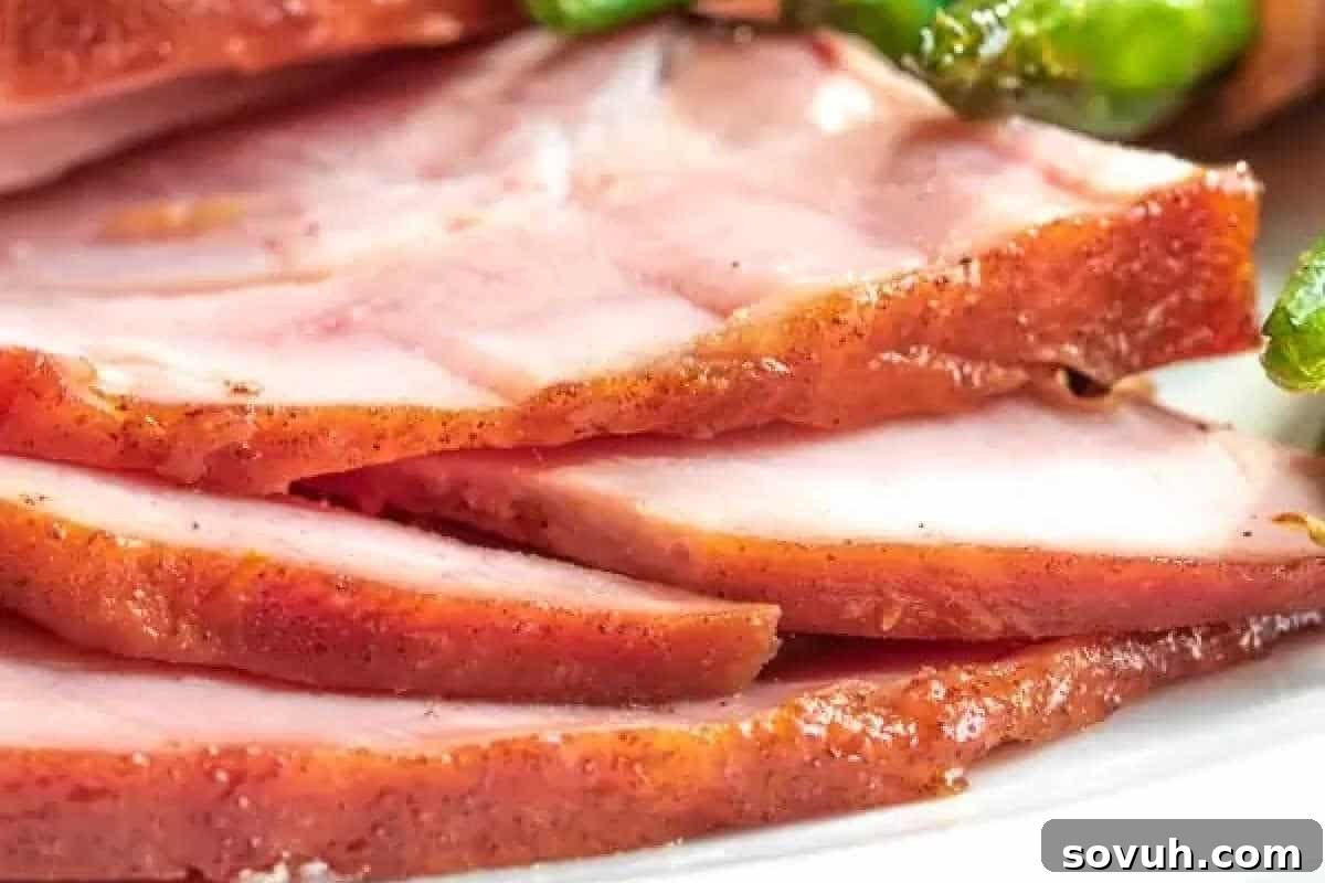 Close-up view of beautifully cooked ham slices, exhibiting a caramelized brown edge, artfully arranged on a plate with vibrant green vegetables providing a fresh backdrop.