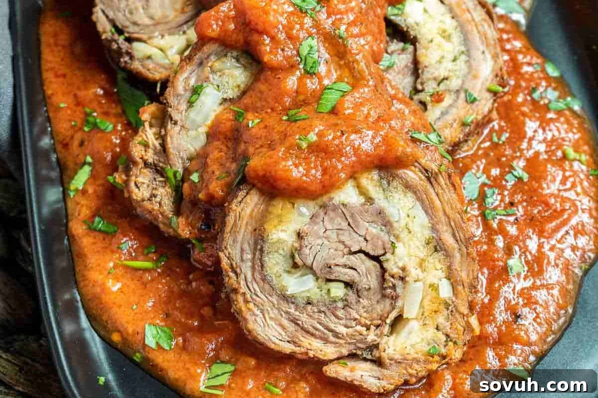 A generous slice of stuffed beef roll, luxuriating under a rich tomato sauce, gracefully garnished with finely chopped herbs on a sophisticated black plate.