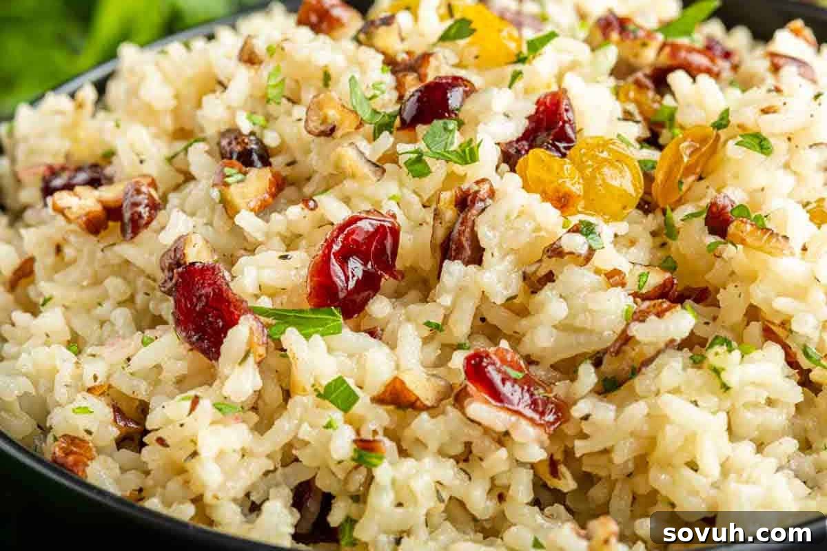 A bowl of rice mixed with chopped pecans, dried cranberries, golden raisins, and garnished with parsley.