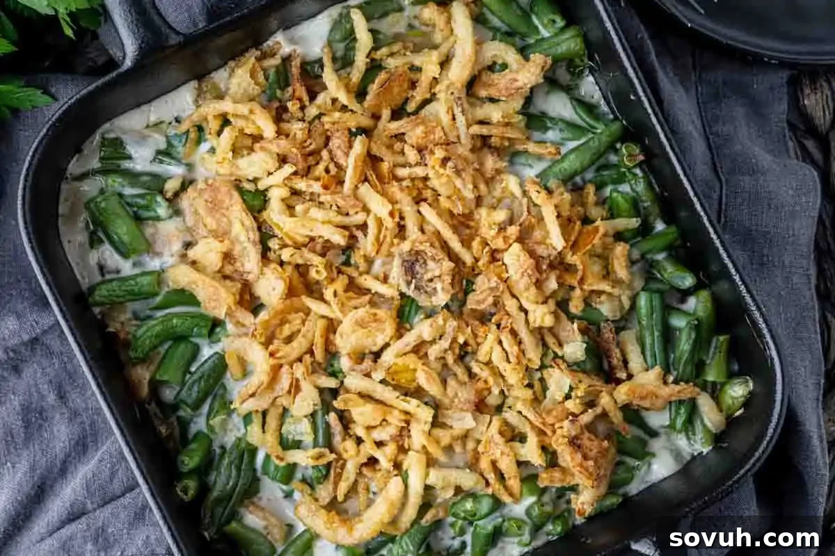 A casserole dish filled with green bean casserole topped with crispy fried onions, set on a dark cloth—an essential addition to the ultimate lineup of Christmas sides for the perfect plate.