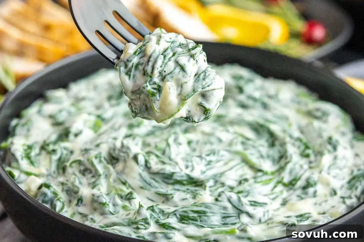 A fork lifts a serving of creamy spinach dip from a black bowl, creating the perfect plate for your Christmas sides and the ultimate lineup of holiday appetizers.