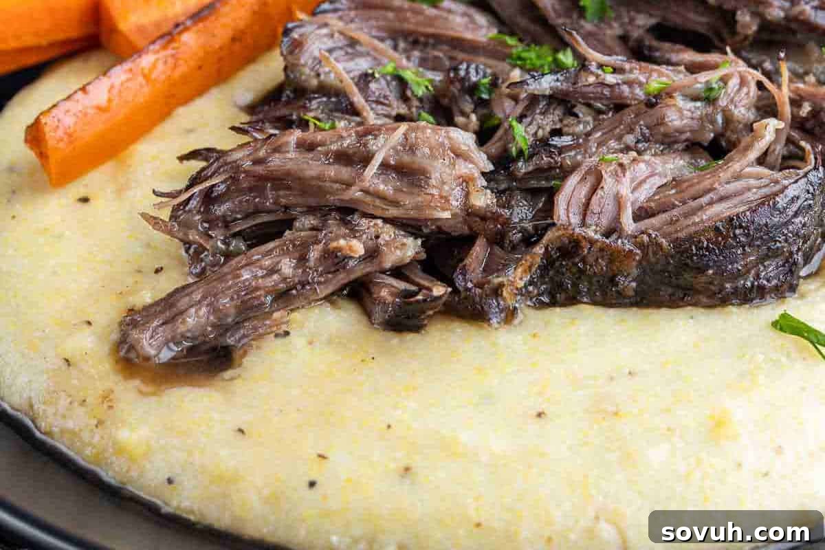 Shredded beef served on creamy polenta, accompanied by roasted carrot sticks, garnished with chopped parsley.