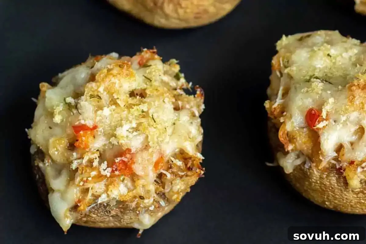 A delectable close-up of oven-baked stuffed mushrooms, generously topped with melted cheese, savory breadcrumbs, and finely diced red peppers. These exquisite bites are ideal as elegant party appetizers for your New Year’s Eve celebration.