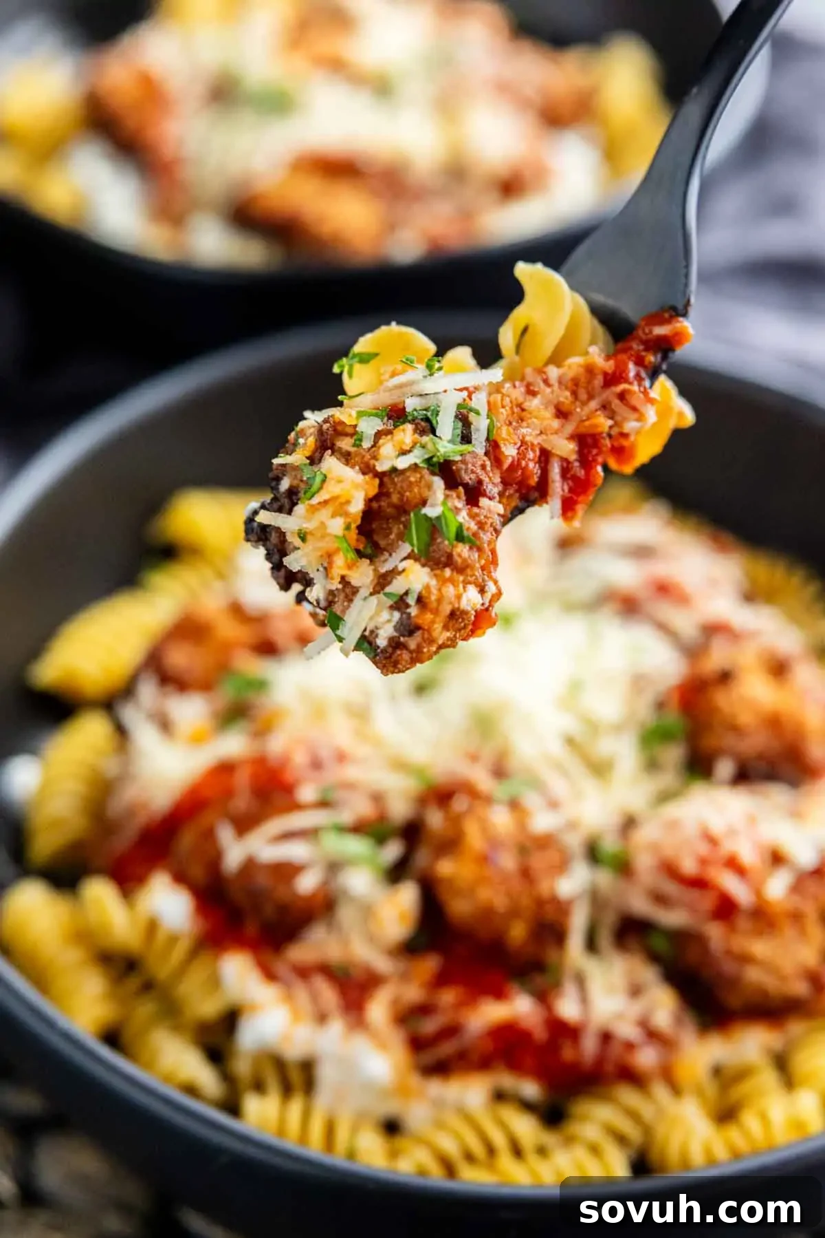 A close-up shot capturing a fork holding a perfect bite of rotini pasta, luscious tomato sauce, and a tender chicken piece, lifted above a full bowl of the easy high protein dinner. The bowl itself is beautifully topped with sauce and melted cheese, making it an enticing option for busy weeknights.