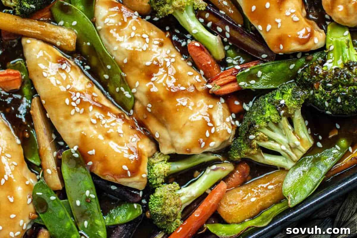 Enjoy one of the best high-protein recipes with chicken breasts glazed in teriyaki sauce, topped with sesame seeds, and served alongside fresh broccoli, carrots, and snap peas—a flavorful addition to your new year recipes collection. A simple sheet pan honey garlic chicken and vegetables meal.