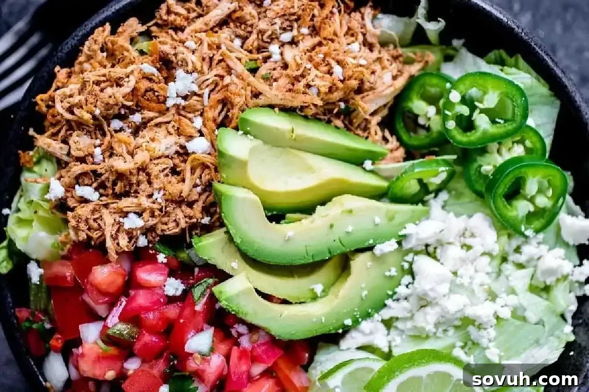 A bowl containing shredded chicken, sliced avocado, jalapeños, pico de gallo, crumbled cheese, lettuce, and lime wedges—one of the best high-protein recipes to add to your new year recipes collection. A quick and customizable chicken taco bowl.