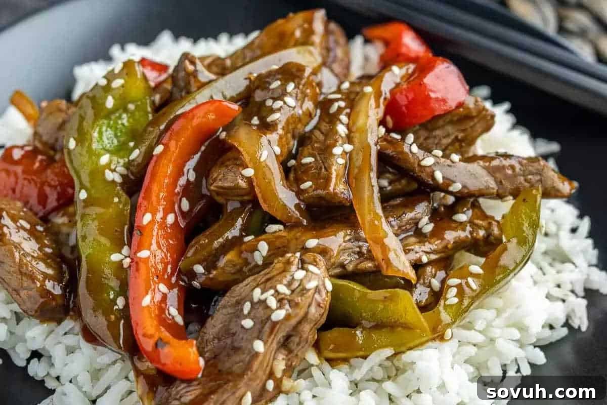 A plate of white rice topped with stir-fried beef, red and green bell peppers, onions, brown sauce, and sprinkled with sesame seeds—one of the best high-protein recipes for a satisfying and flavorful meal. A quick and tasty homemade pepper steak stir fry.