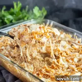 A close-up of a serving of cheesy French Onion Chicken Bake with crispy fried onions being lifted from a glass baking dish.