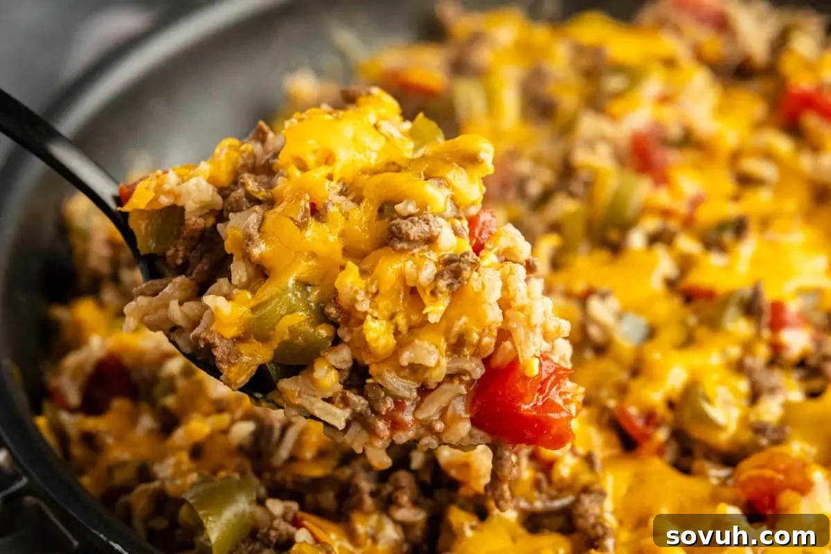 A close-up of a cheesy ground beef and rice skillet with bell peppers and tomatoes, all cooked together for an easy one pan unstuffed peppers meal. The melted cheese creates a delicious golden crust.