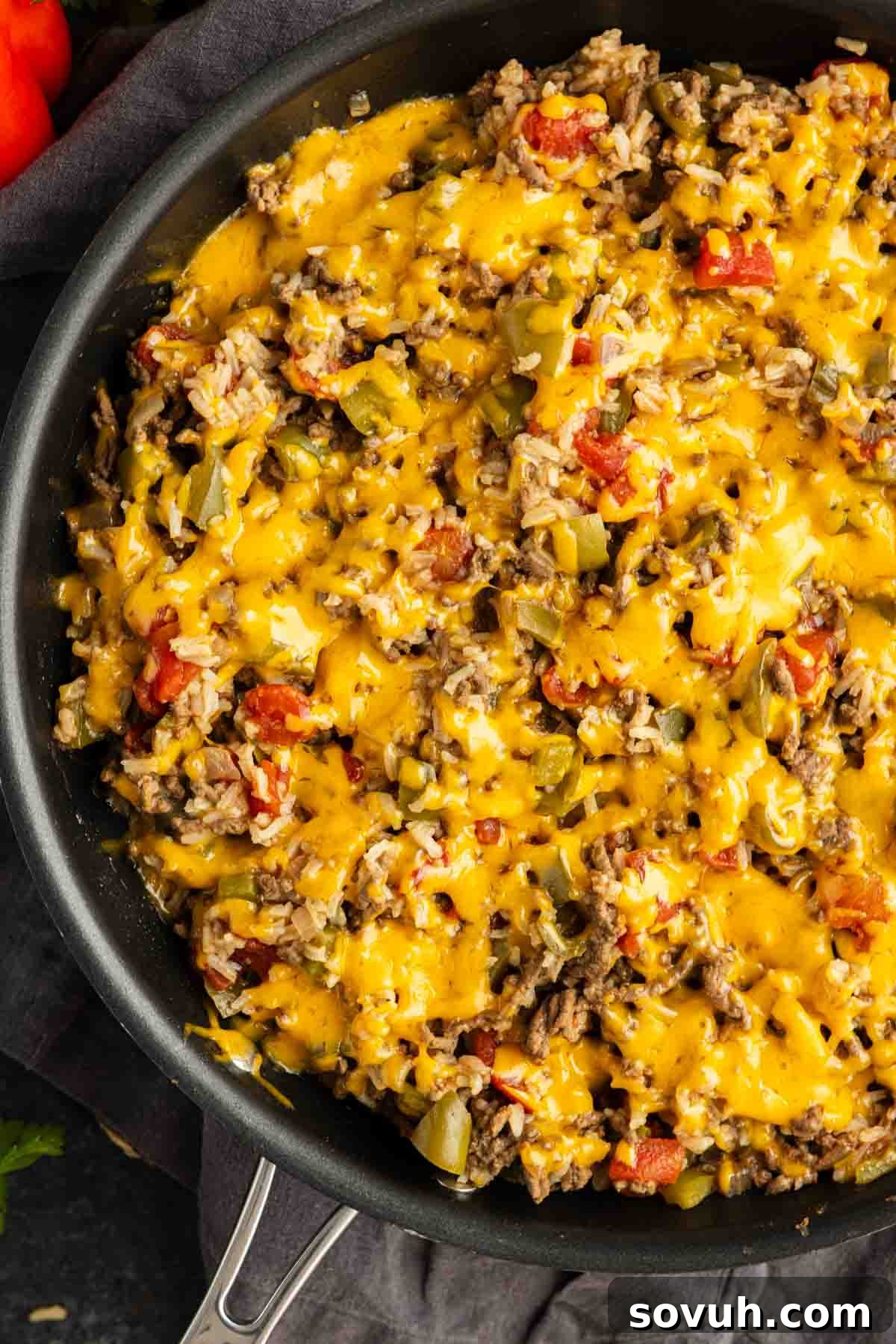 A hearty and delicious one-pan unstuffed peppers dish, presented in a cast iron skillet. It's brimming with flavorful ground beef, perfectly cooked rice, diced tomatoes, tender green bell peppers, and topped with a generous layer of glistening melted cheddar cheese, ready to be served.