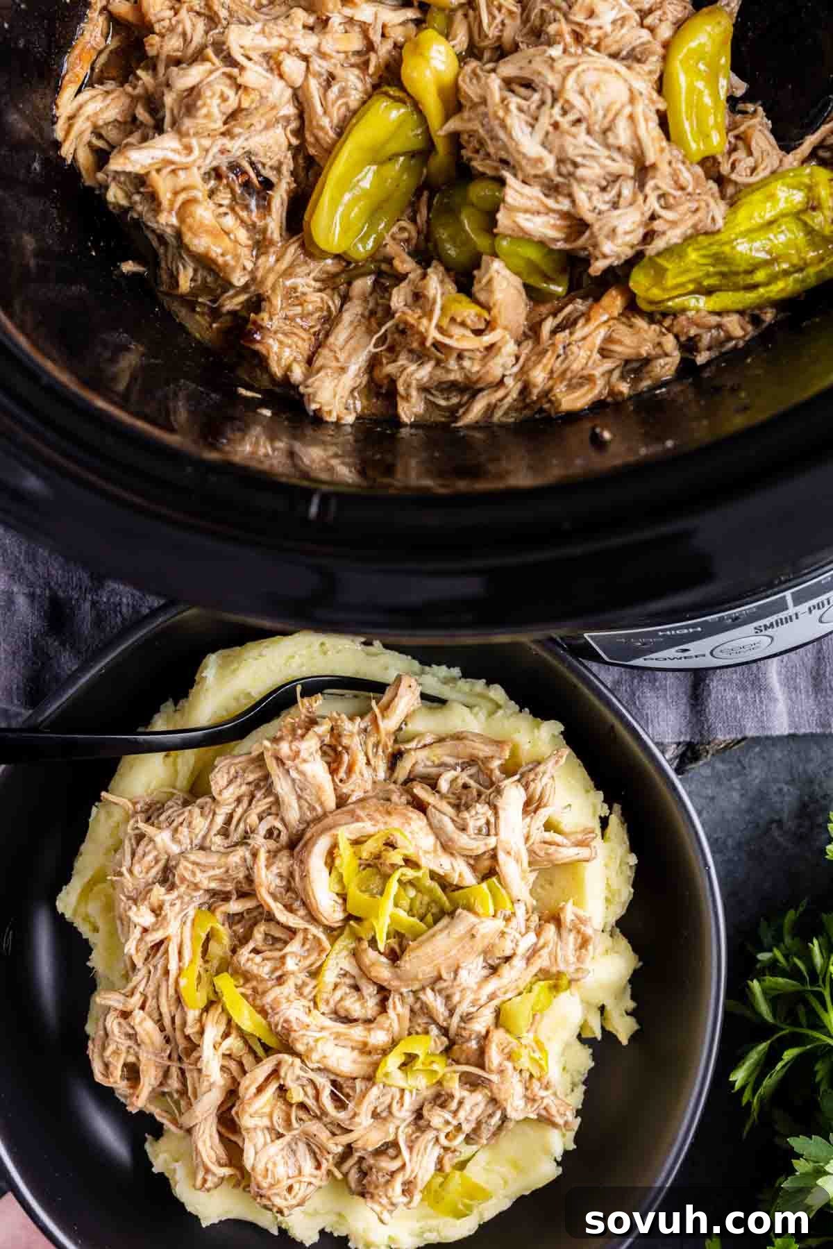 Slow Cooker Mississippi Chicken—tender, pepperoncini chicken slow-cooked in a crockpot—served over mashed potatoes in a black bowl with a fork. It's the ultimate dump and go crockpot meal for cozy comfort food nights.