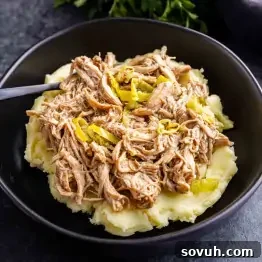 A black bowl filled with mashed potatoes topped with shredded meat and sliced peppers, with a fork on the side.