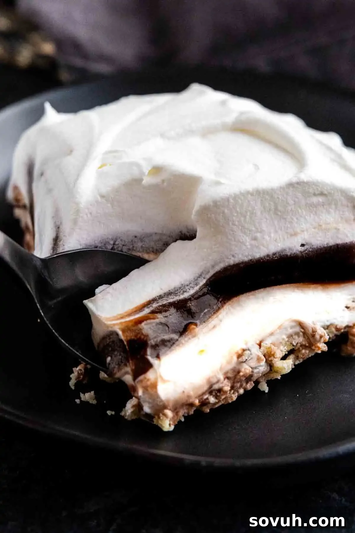 Decadent Chocolate Dream 2 A close-up of a layered chocolate pudding dessert with whipped cream, rich chocolate, and a crumbly crust on a black plate, as a spoon takes a bite.