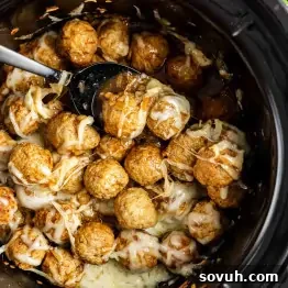 Meatballs topped with melted cheese and flavored with French onion soup mix in a slow cooker, with a serving spoon resting among these easy appetizer meatballs.