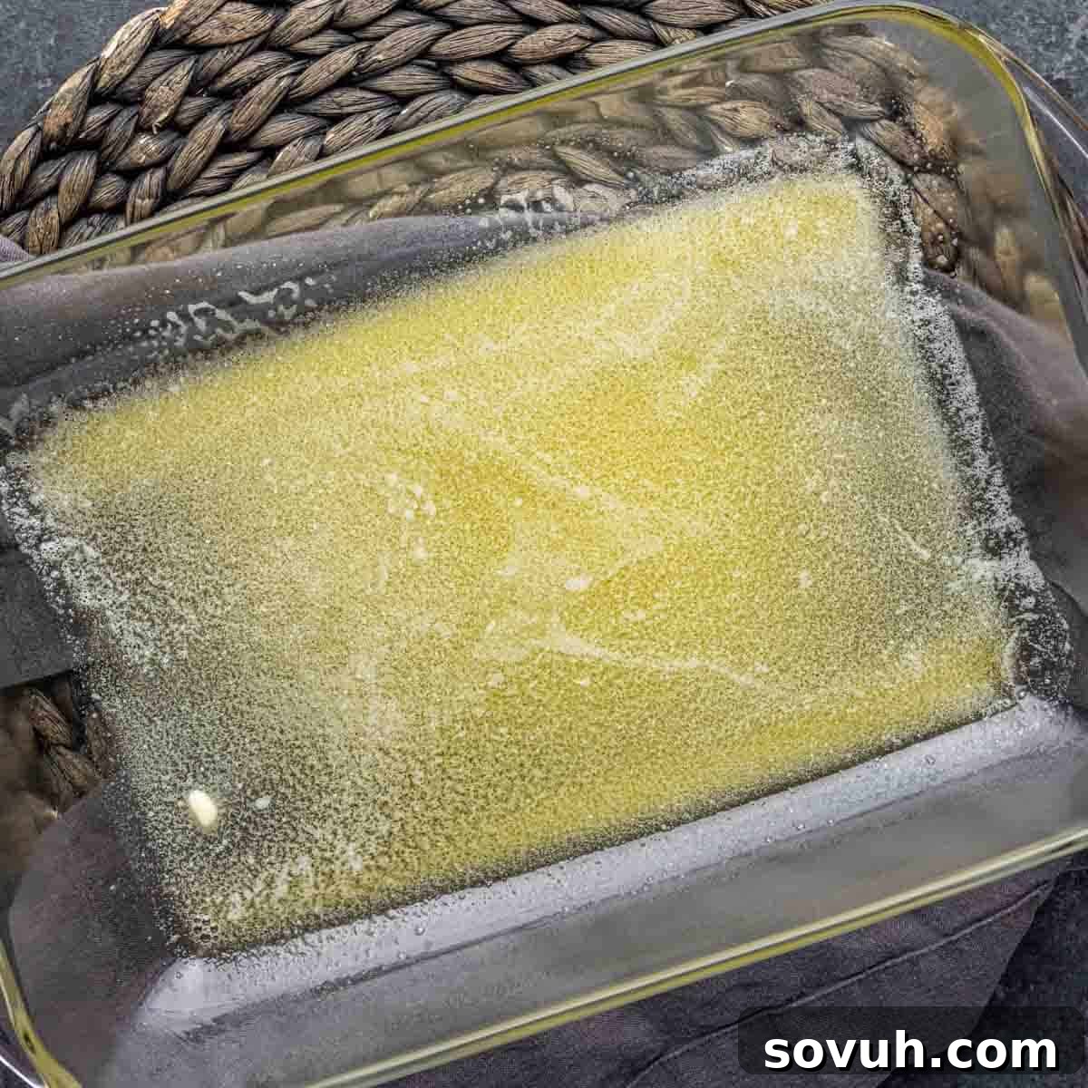 A glass baking dish with a shimmering layer of melted butter, preparing the base for Oreo Magic Bars.