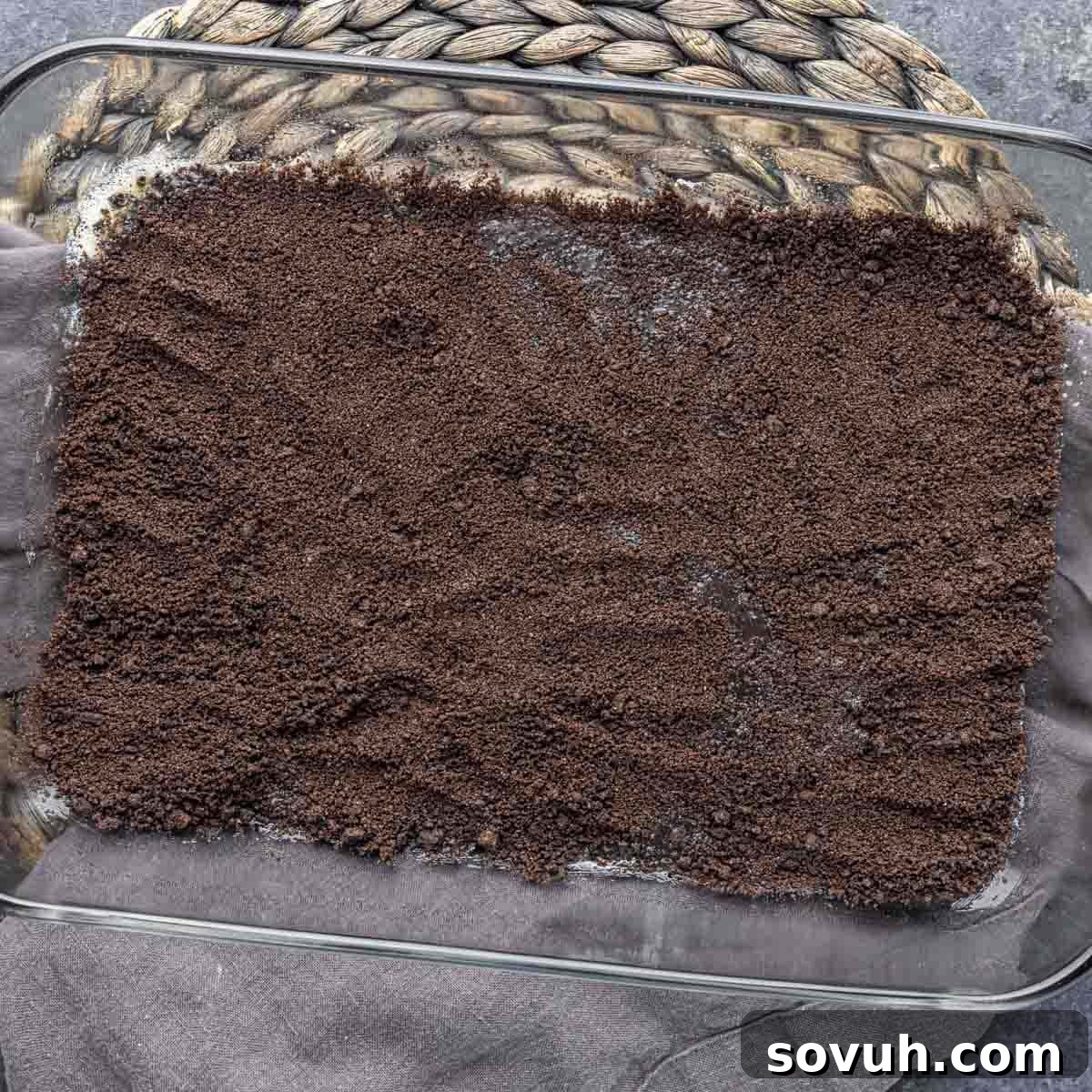 A baking dish filled with an even layer of crushed Oreo crumbs, forming the delicious crust for Oreo Magic Bars.