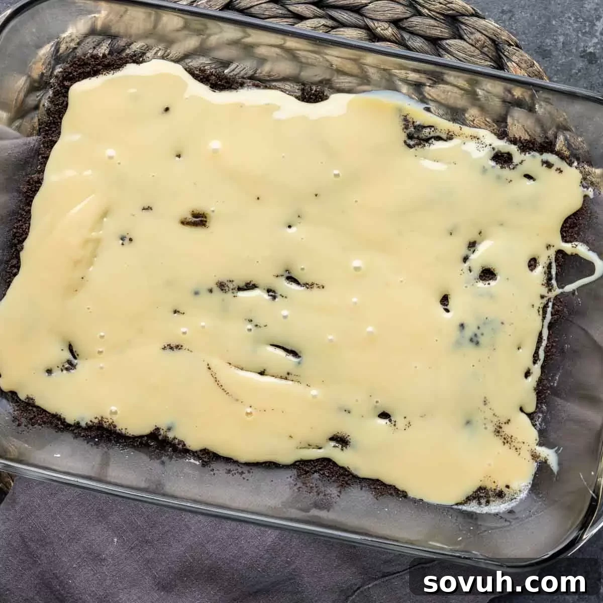 A glass baking dish now featuring a smooth layer of sweetened condensed milk over the Oreo crust, ready for the next delicious additions.