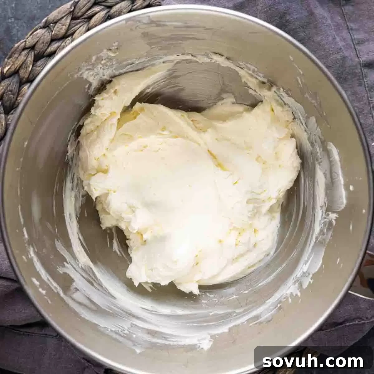 Creamy, softened cream cheese being whipped in a metal mixing bowl, ready for mini cheesecake batter preparation.