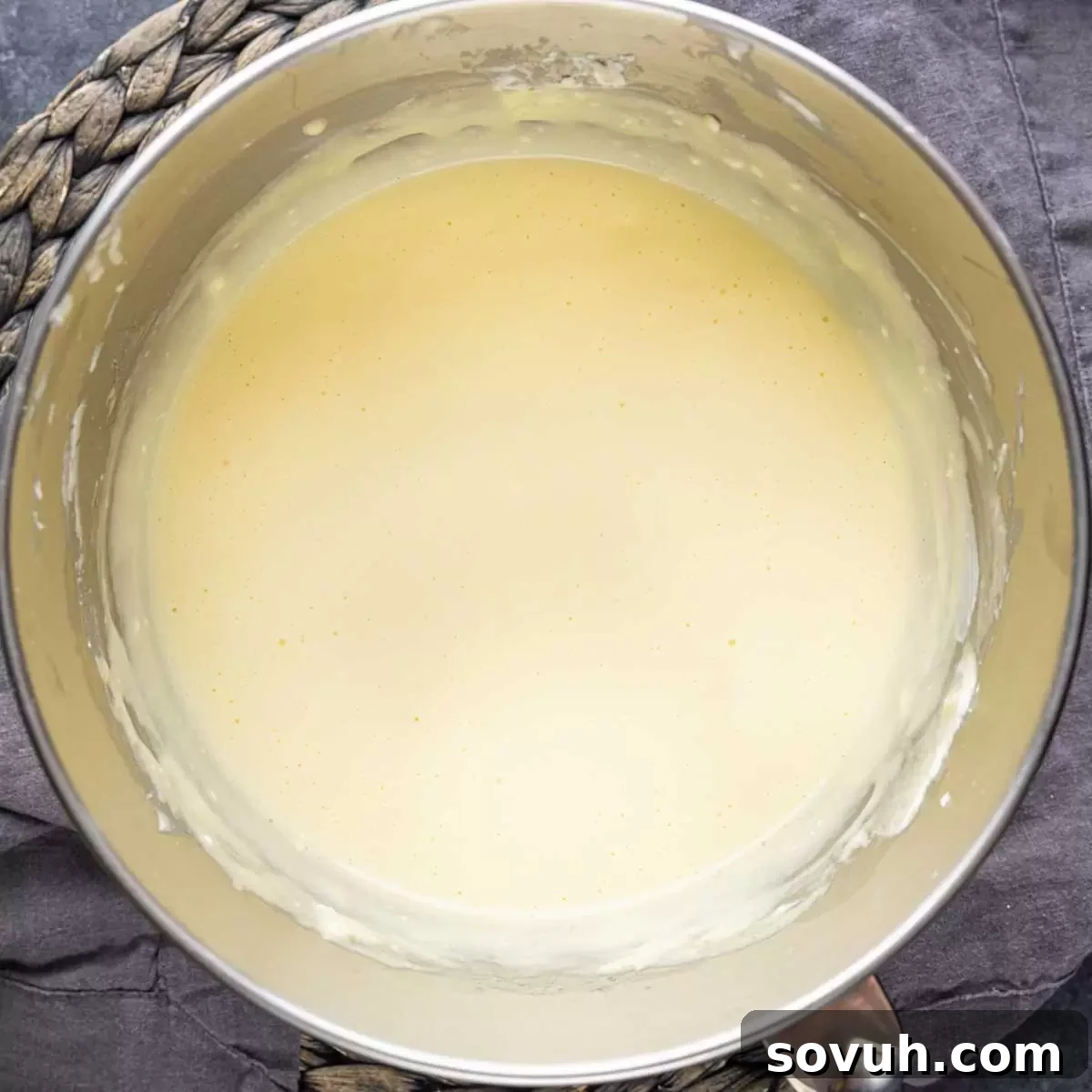 A metal mixing bowl filled with smooth, creamy mini cheesecake batter, ready to be poured into muffin cups.