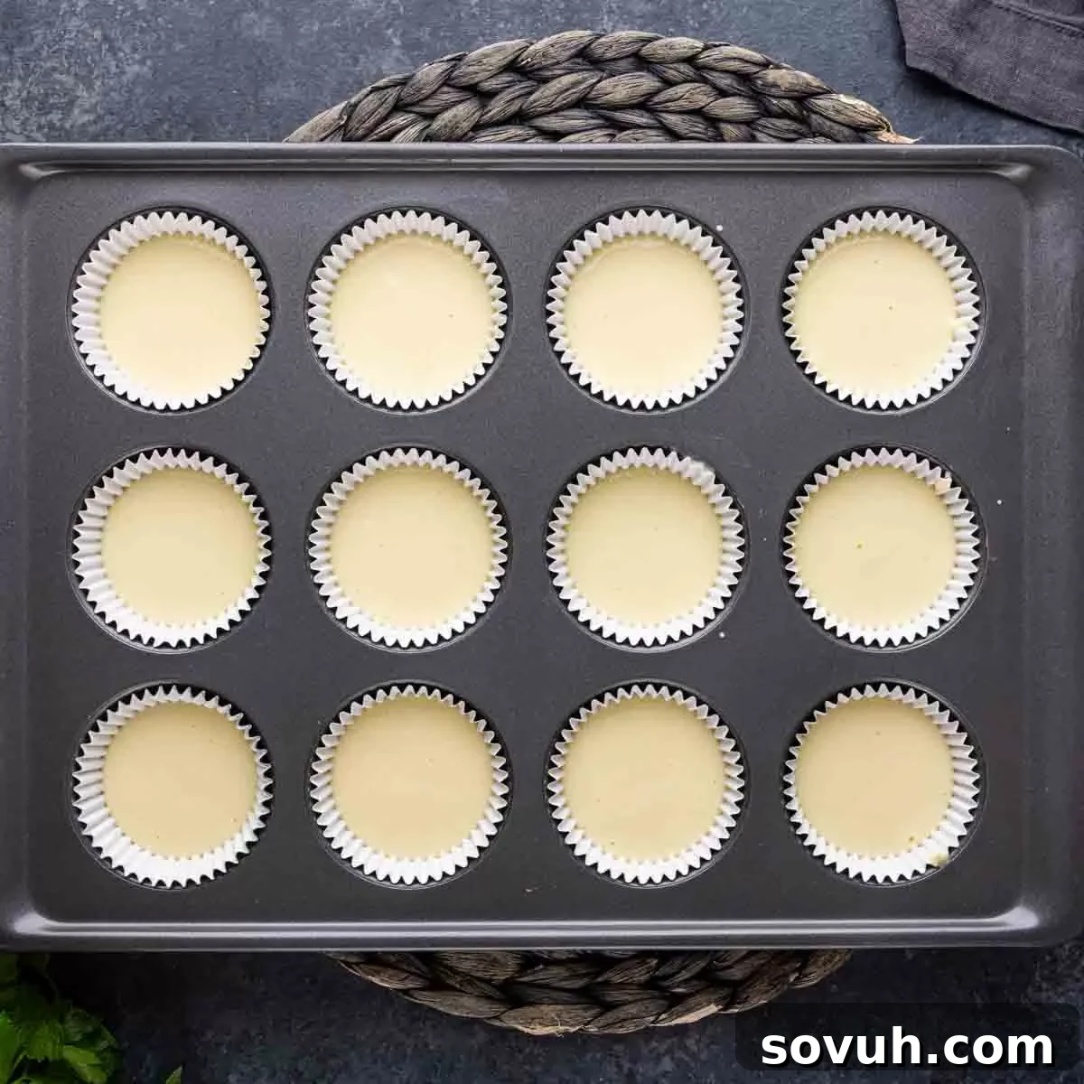 A muffin tin generously filled with unbaked mini cheesecake batter in individual cupcake liners, ready for the oven.