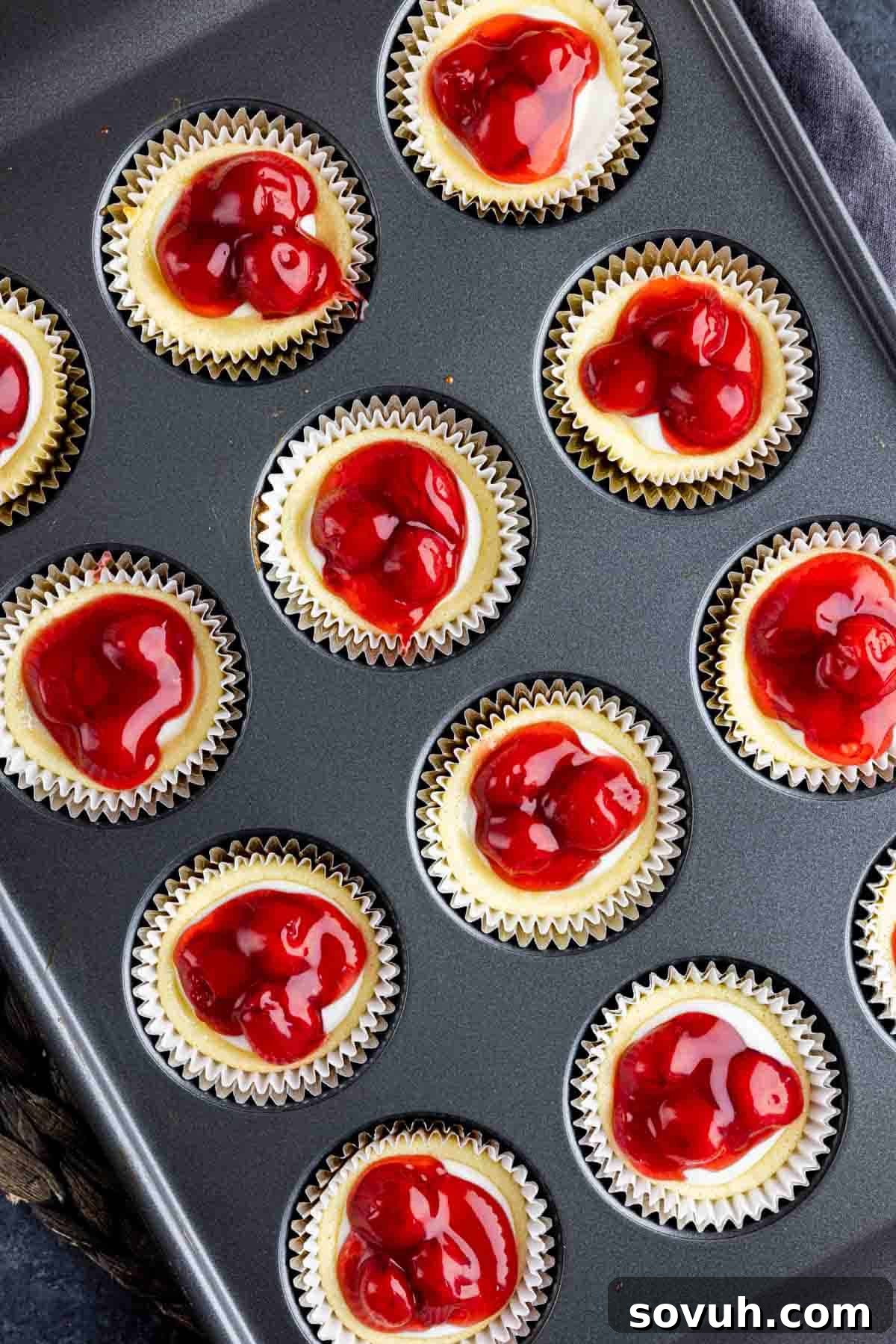A close-up shot of individual cherry mini cheesecakes, baked to perfection and topped with sweet cherry filling in a muffin tin.