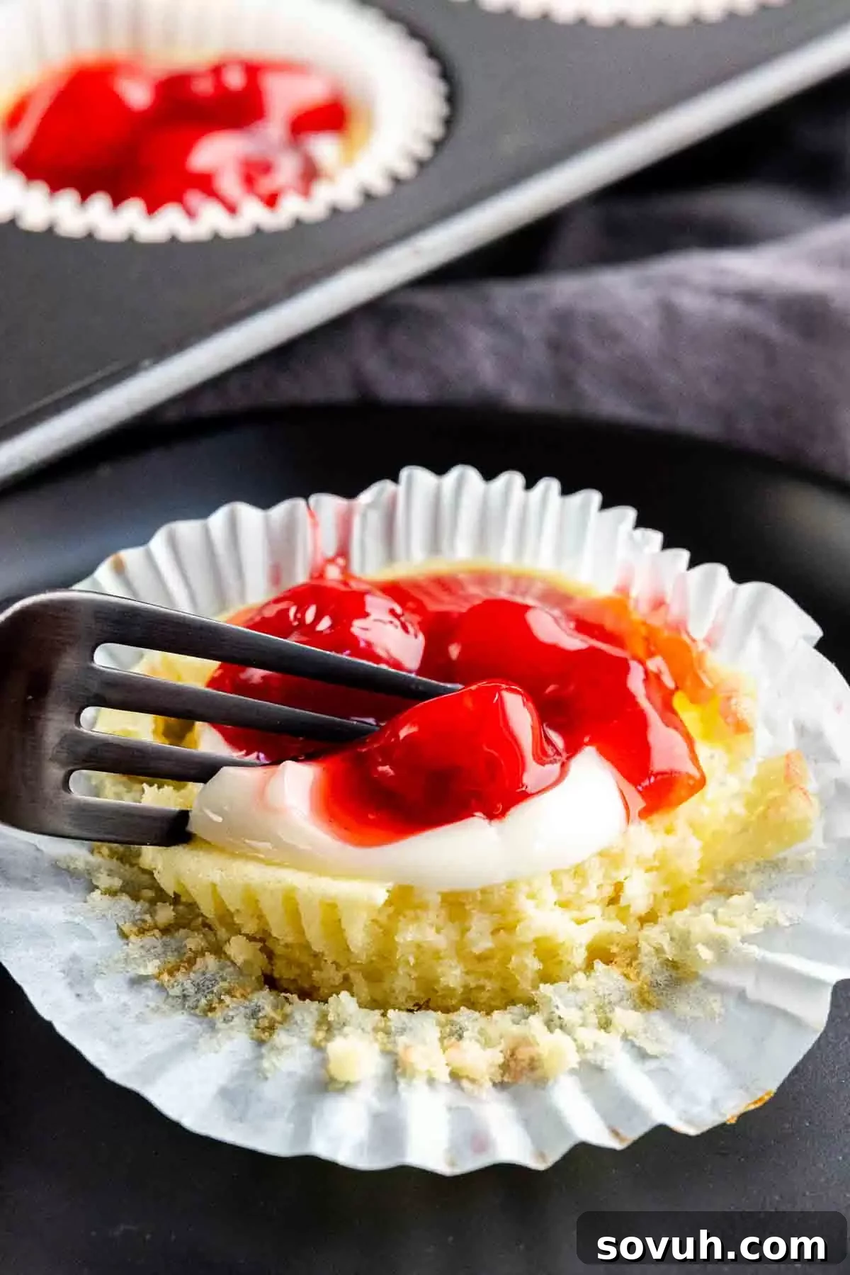 A fork taking a bite out of a creamy, individual mini cheesecake topped with cherry filling, highlighting its perfect texture.