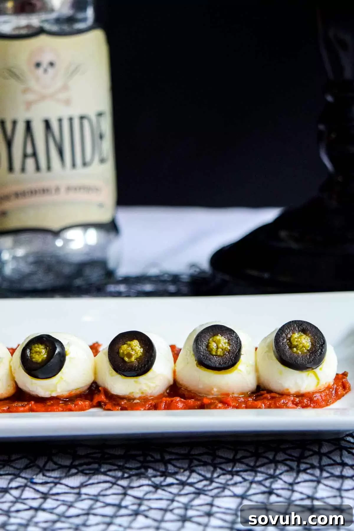 A plate of Halloween eyeballs made with mozzarella, olives, and pesto, on a red tomato base.