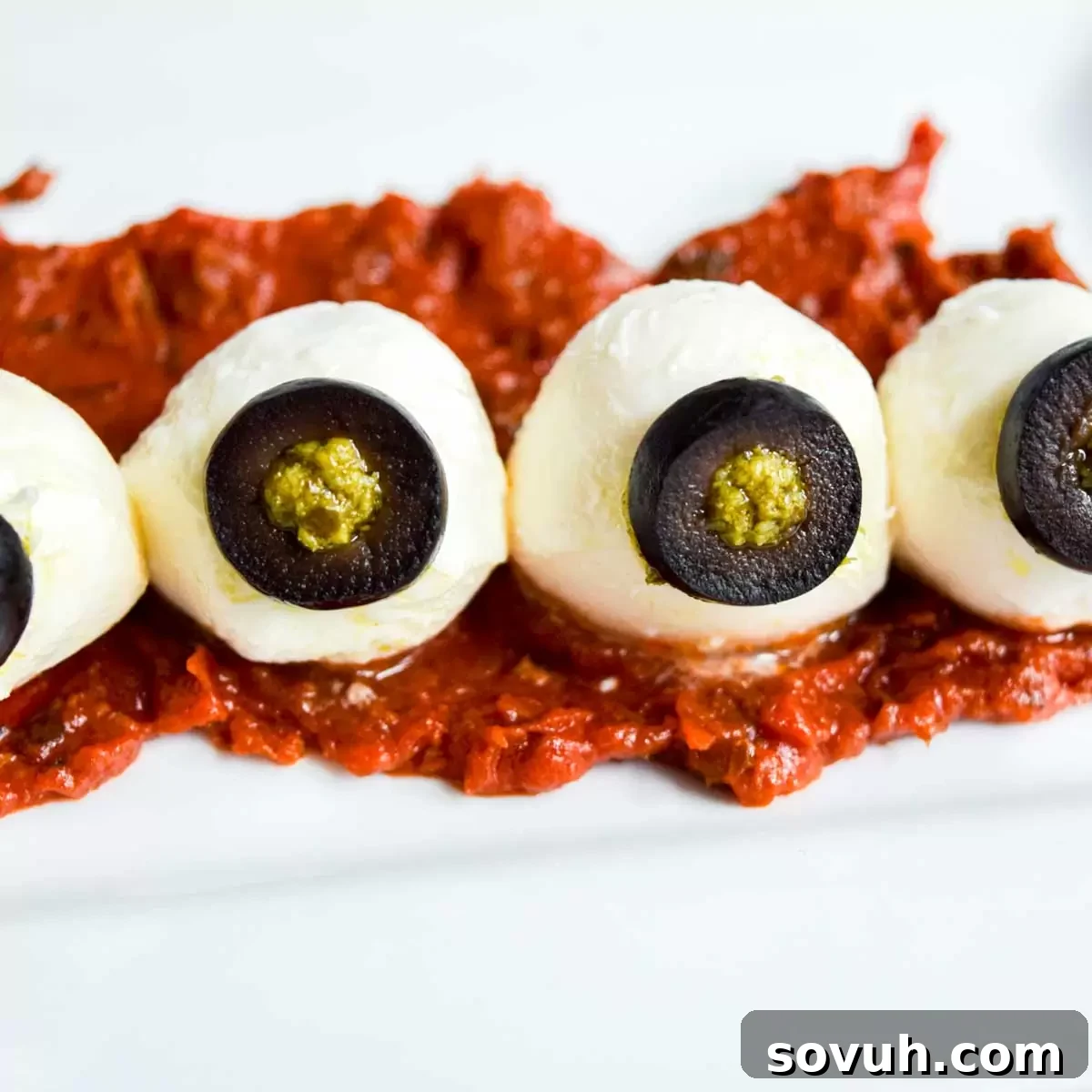 A plate of mozzarella eyeballs with green pesto irises and black olive pupils, ready for a Halloween party.