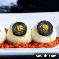 Three mozzarella balls with black olive eyes, resembling Halloween eyeballs, on a white plate.