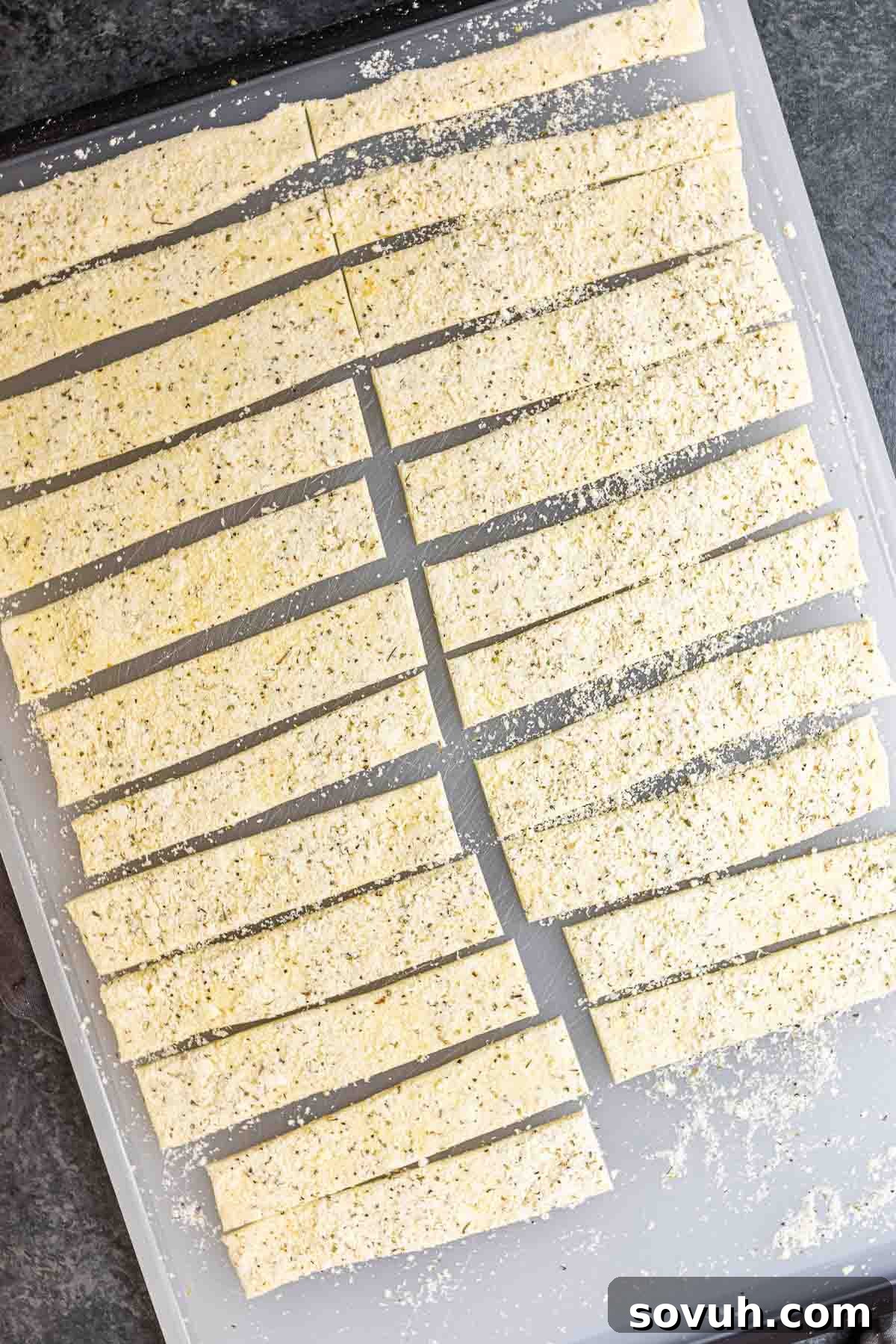 Puff pastry dough being cut into strips, ready for twisting into cheese twists.