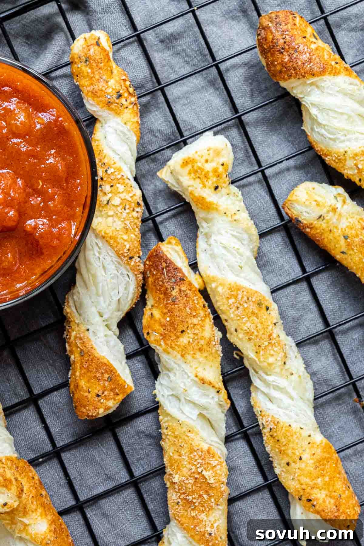 Freshly baked cheese twists cooling on a rack, with a bowl of dipping sauce nearby.