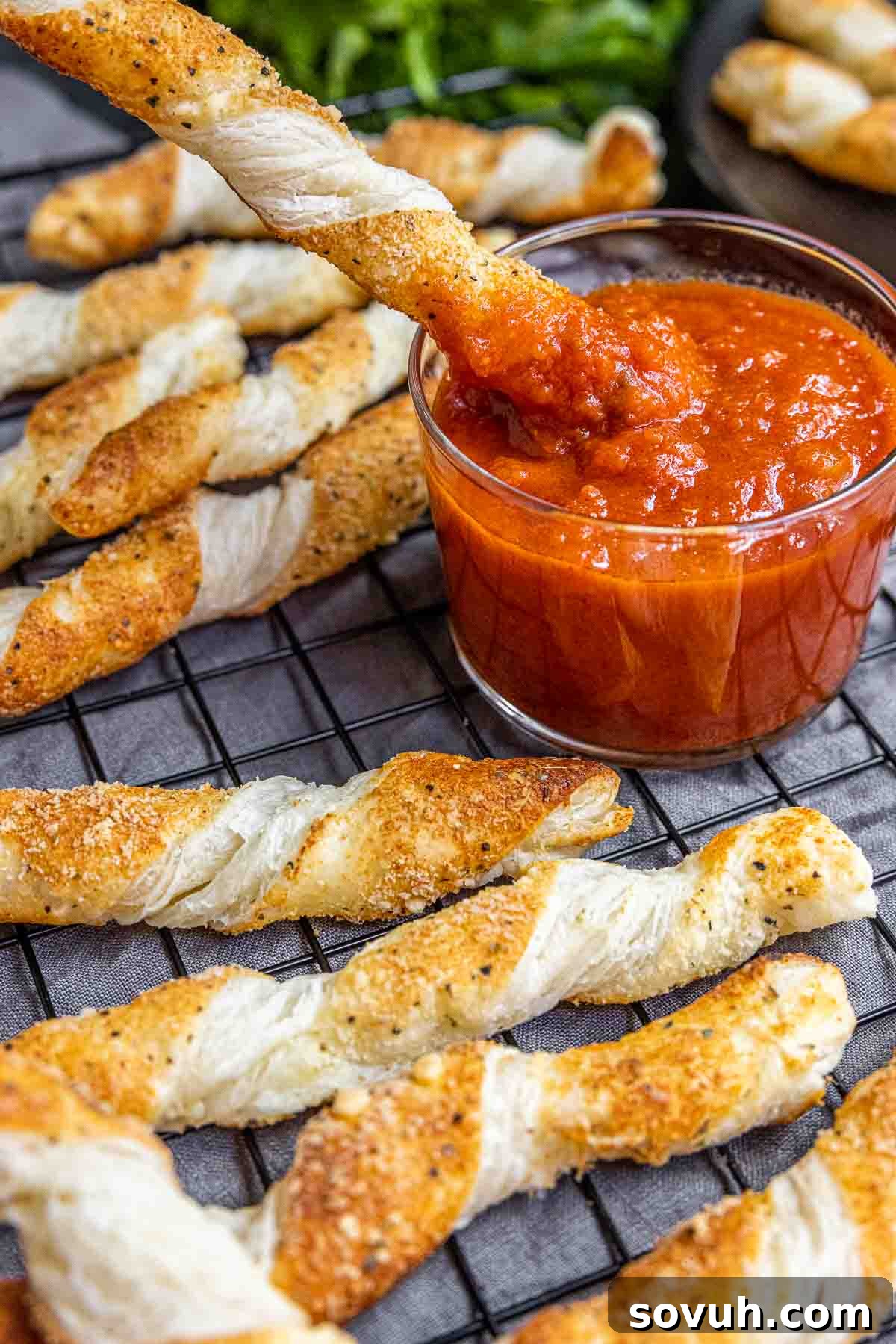 Close-up of a cheese twist being dipped into a rich, flavorful sauce.