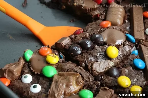 A close-up of a cut Witch's Brew Brownie, revealing its rich chocolate interior and colorful, melted Halloween candy pieces.