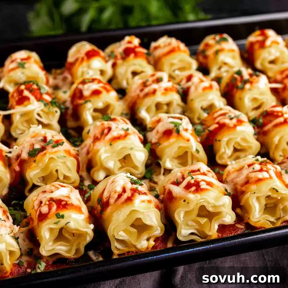 A tray of golden-brown mini lasagna appetizers topped with fresh tomato sauce and grated parmesan cheese, ready to serve.