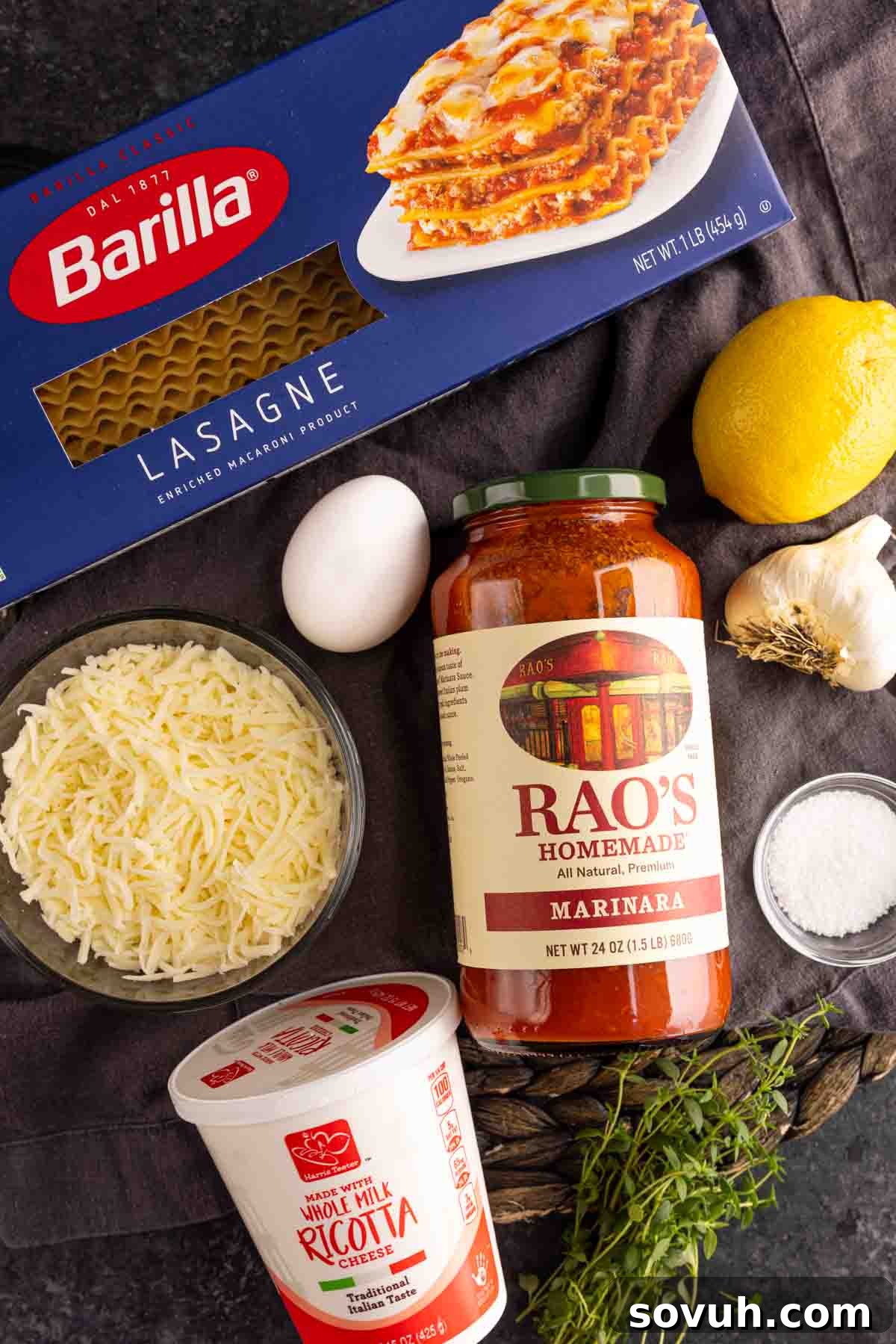 A selection of fresh ingredients including whole milk ricotta, a lemon, thyme, an egg, and a block of mozzarella, neatly arranged on a rustic wooden table, ready for making mini lasagna appetizers.
