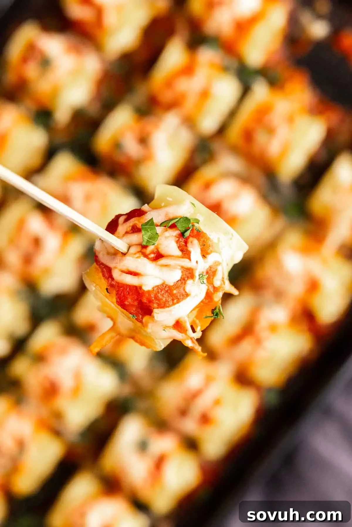 A hand holding a toothpick, picking up a single mini lasagna appetizer from a tray, showing its bite-sized appeal.