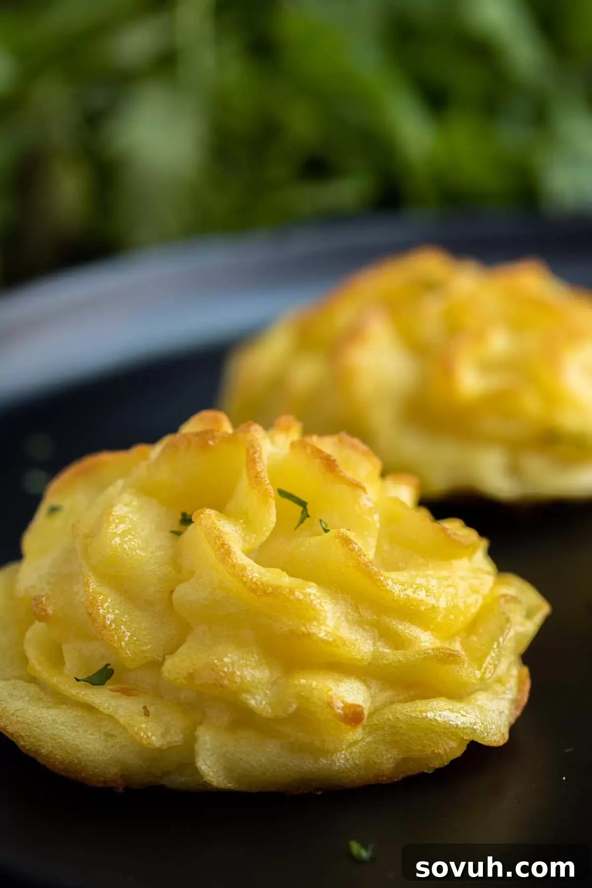 Baked Duchess Potatoes on a black plate, garnished with fresh parsley.