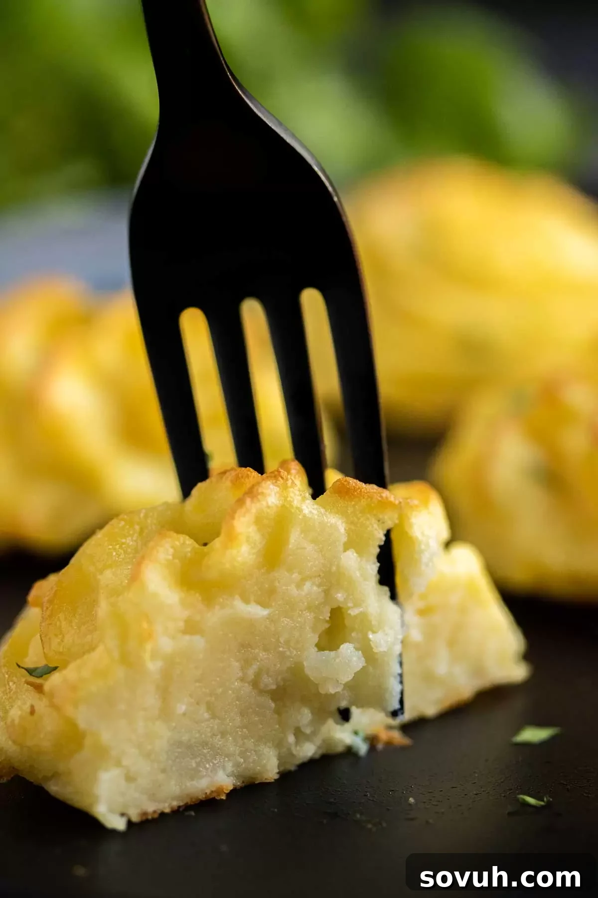 A black fork gently piercing a baked Duchess Potato on a black surface.