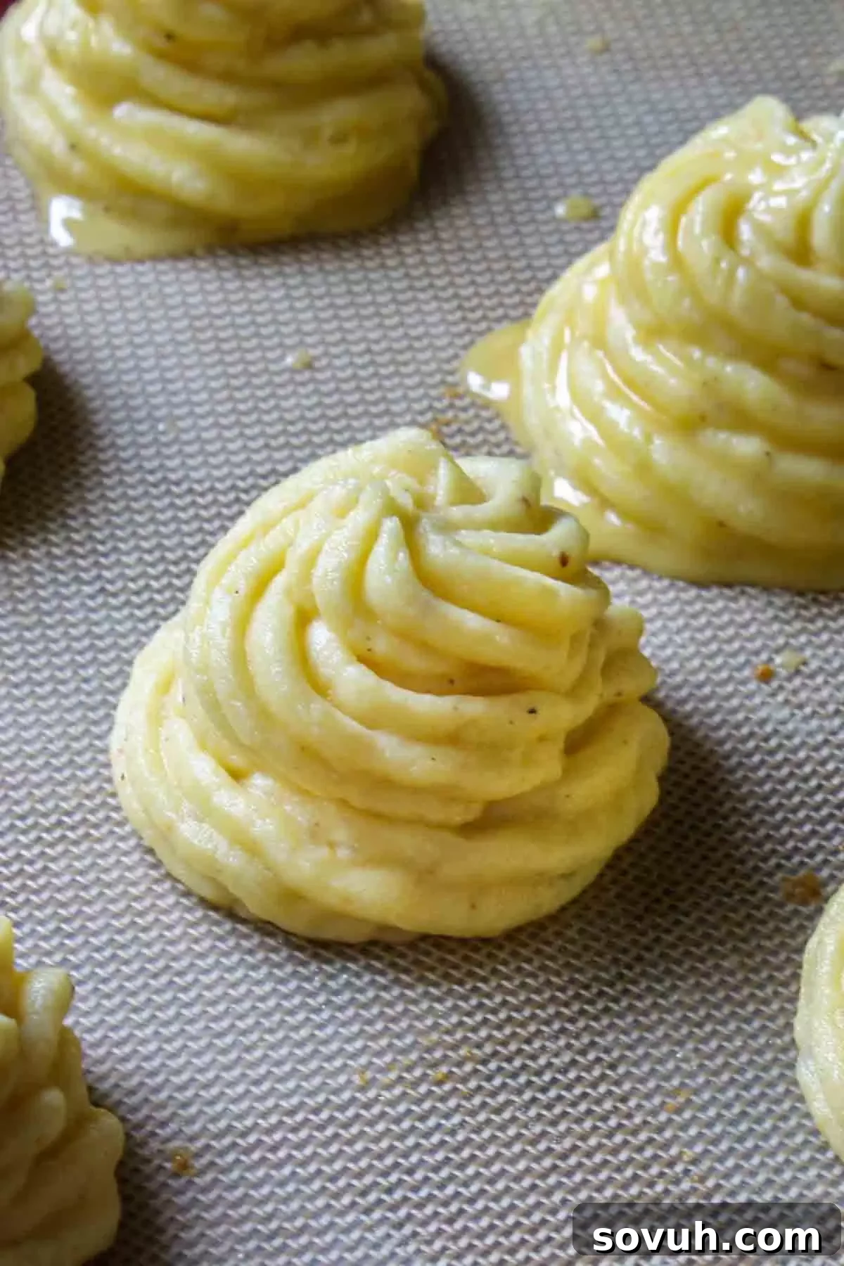 Piping Duchess Potatoes onto a baking sheet, showcasing the elegant swirl pattern.