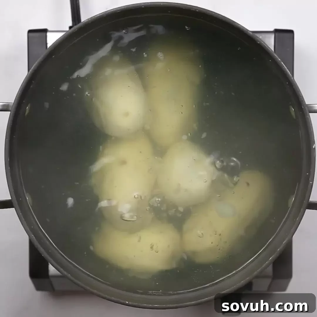 Boiling peeled potatoes in a large pot on a stove, the first step for Duchess Potatoes.