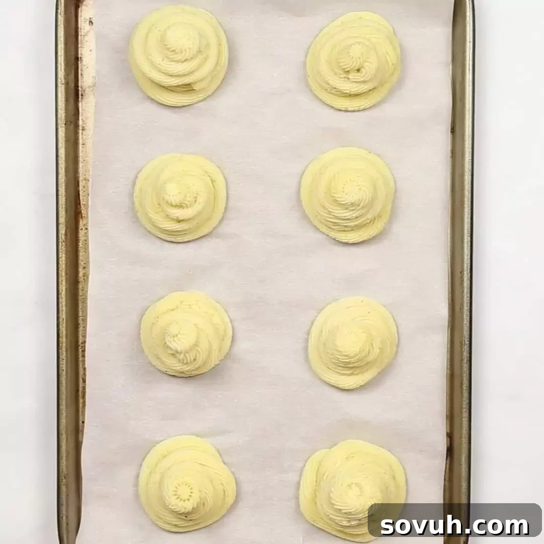 A baking sheet filled with intricately piped Duchess Potatoes, ready for freezing.