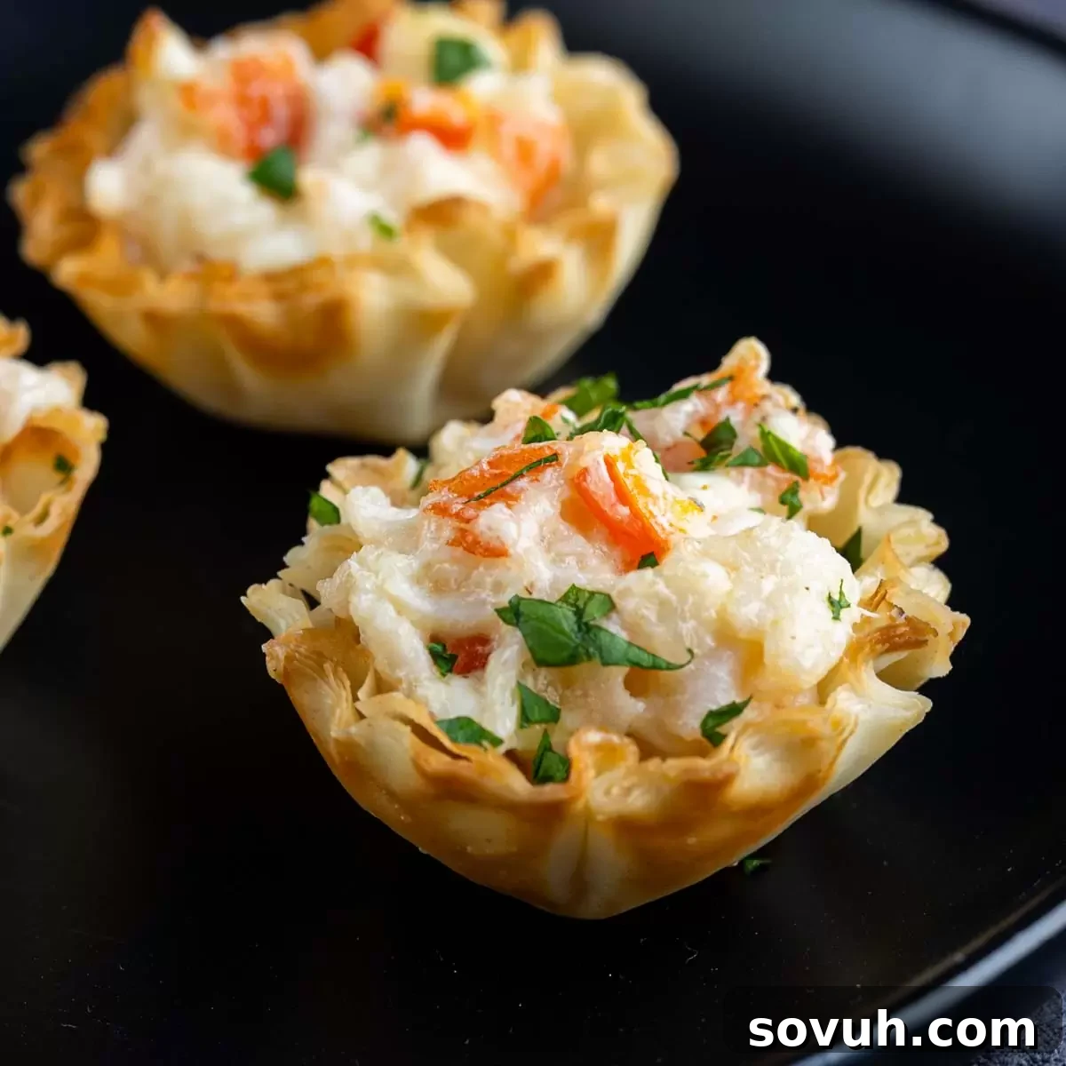 Crab puff pastry cups with crabmeat and parsley on a black plate, ready to be served as an appetizer.