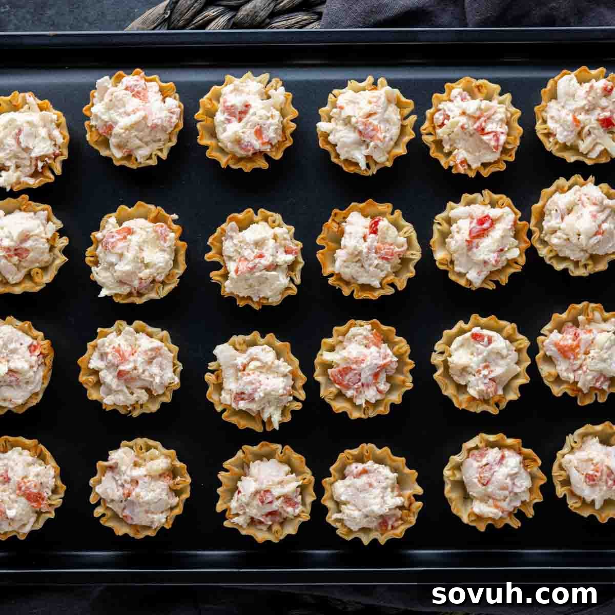 A baking tray filled with phyllo cups, each generously spooned with the creamy crab mixture, ready for the oven.