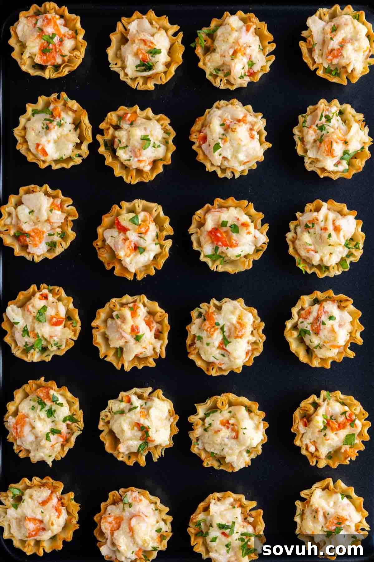 A black serving tray adorned with an array of crispy Baked Crab Bites, garnished with fresh herbs, ready for guests.