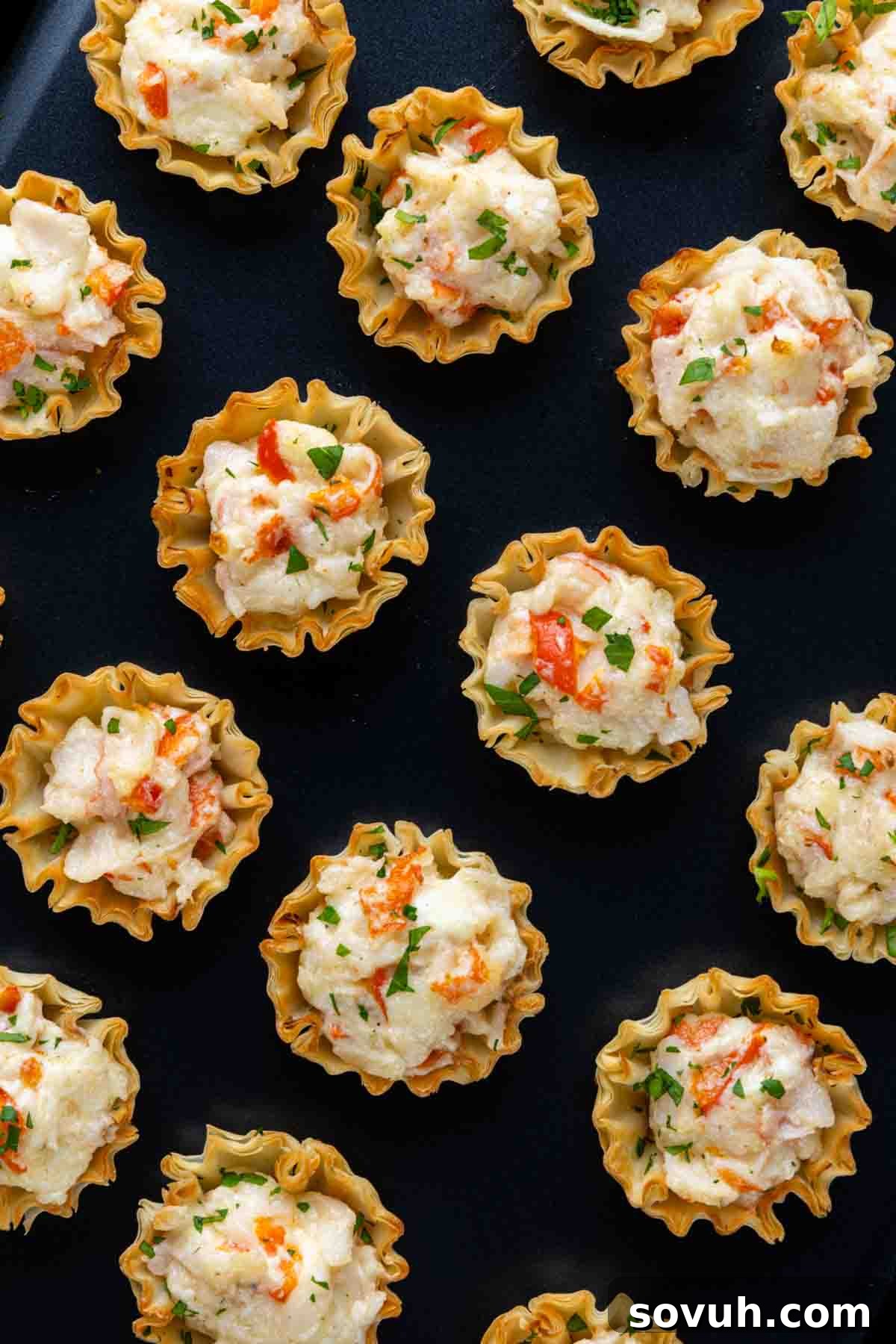 A black tray showcasing a generous arrangement of Baked Crab Bites, artfully presented for a party setting.