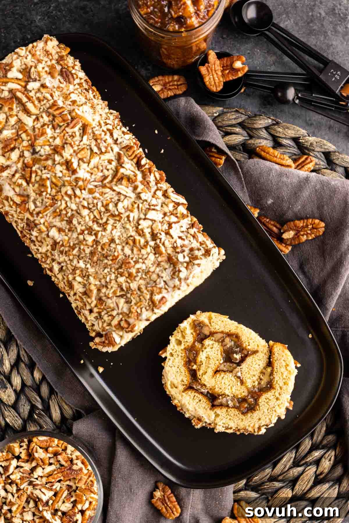 Pecan Pie Cake Roll on a platter with one slice and whole pecans scattered
