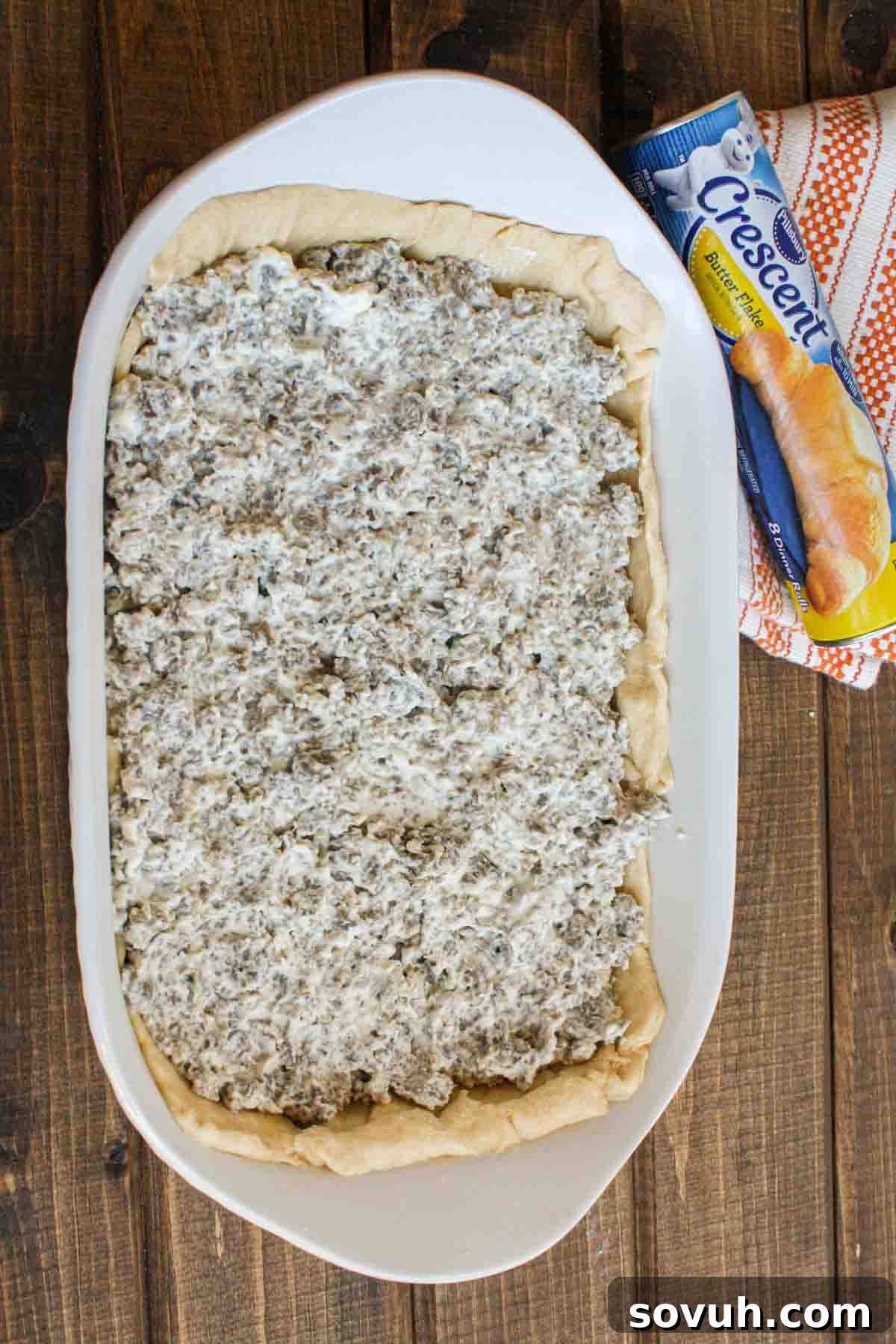 A layer of sausage and cream cheese spread over crescent roll dough in a baking dish for the casserole.