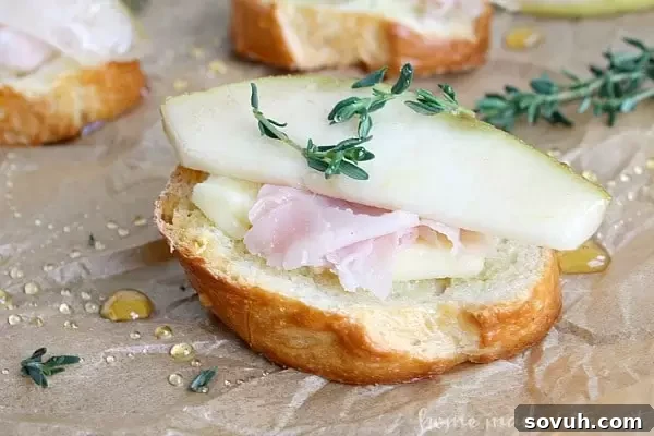 Three Havarti, Ham, and Pear Crostini artfully arranged on a serving board, garnished with fresh thyme sprigs and a visible honey drizzle, showcasing their elegant presentation.