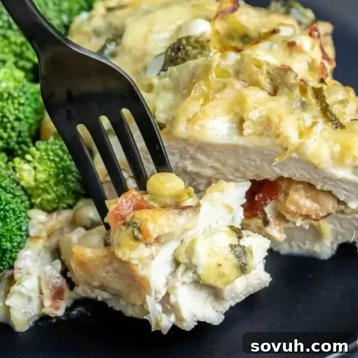 A fork lifting a bite-sized piece of creamy, cheesy chicken and artichoke bake with visible broccoli on the side on a black plate.