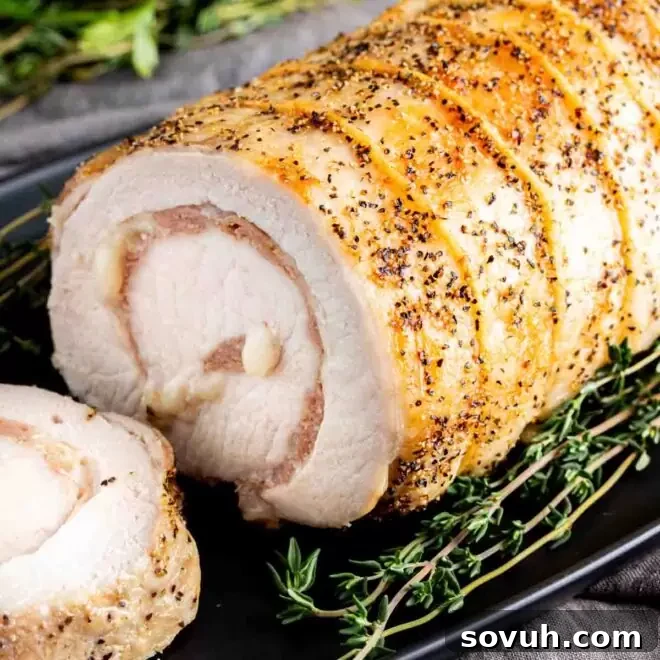 A Provolone and Prosciutto Stuffed Pork Loin on a black plate with fresh thyme sprigs, beautifully presented.